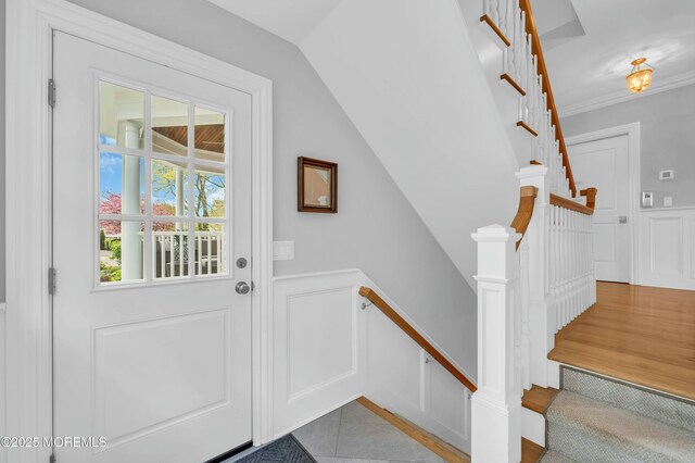 doorway to outside featuring vaulted ceiling, wainscoting, ornamental molding, and a decorative wall
