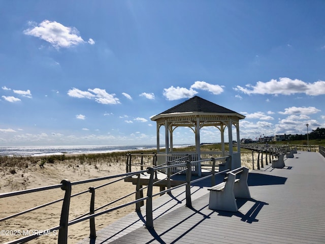 view of dock with a water view, a beach view, and a gazebo