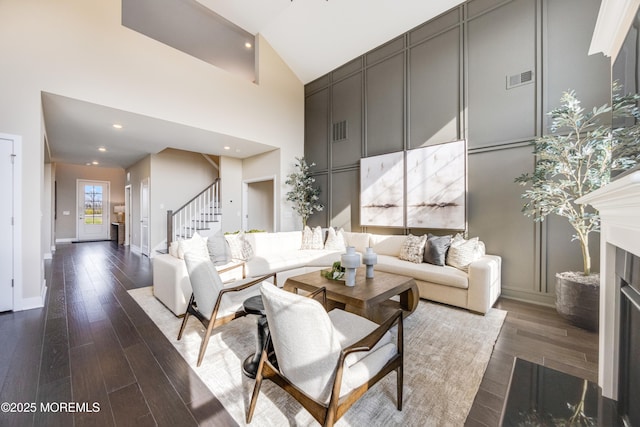 living area featuring wood finished floors, high vaulted ceiling, a fireplace, visible vents, and stairs