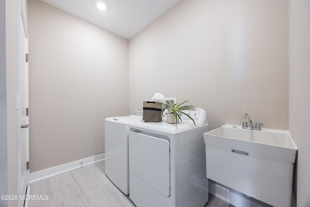 laundry area featuring a sink, laundry area, washing machine and clothes dryer, baseboards, and light wood-style floors