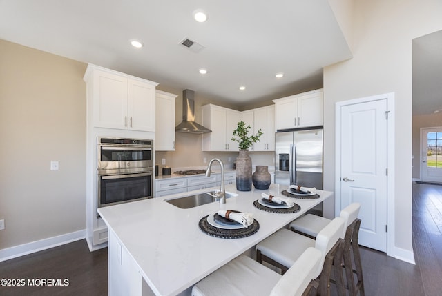 kitchen with a sink, stainless steel appliances, visible vents, wall chimney range hood, and dark wood-style floors