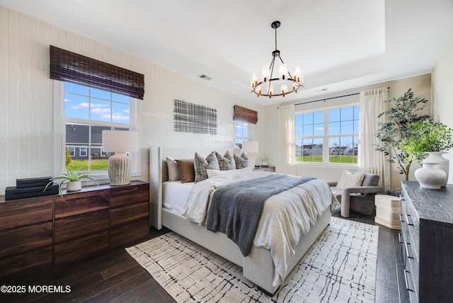 bedroom with a raised ceiling, hardwood / wood-style floors, an inviting chandelier, and visible vents