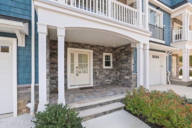 entrance to property featuring stone siding, an attached garage, and covered porch