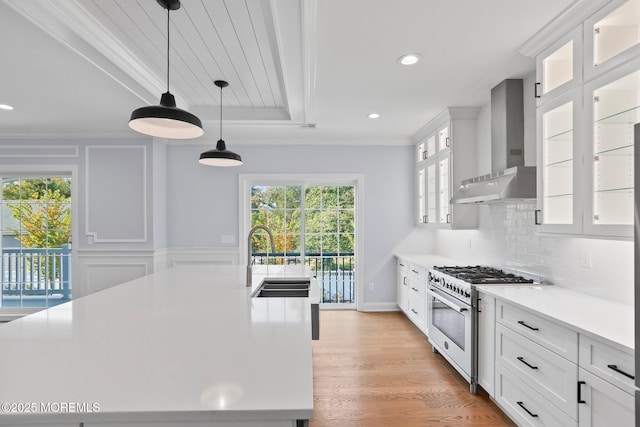 kitchen with white cabinets, light countertops, high end stove, wall chimney range hood, and a sink