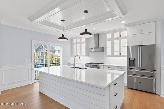 kitchen featuring stainless steel appliances, a tray ceiling, light countertops, wall chimney range hood, and a sink