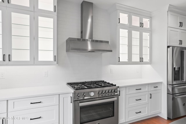 kitchen featuring light countertops, wall chimney exhaust hood, appliances with stainless steel finishes, and decorative backsplash