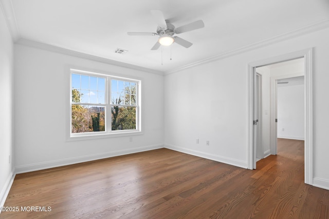 empty room featuring wood finished floors, visible vents, a ceiling fan, ornamental molding, and baseboards