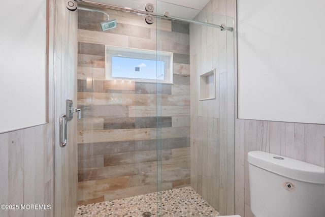 bathroom featuring a shower stall, toilet, and wooden walls
