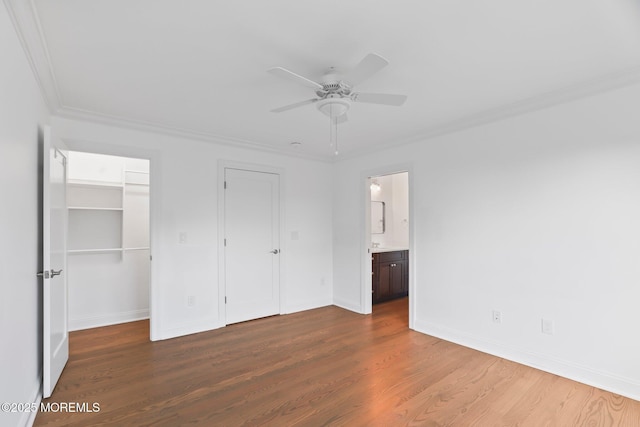 unfurnished bedroom featuring wood finished floors, a ceiling fan, ensuite bath, crown molding, and baseboards