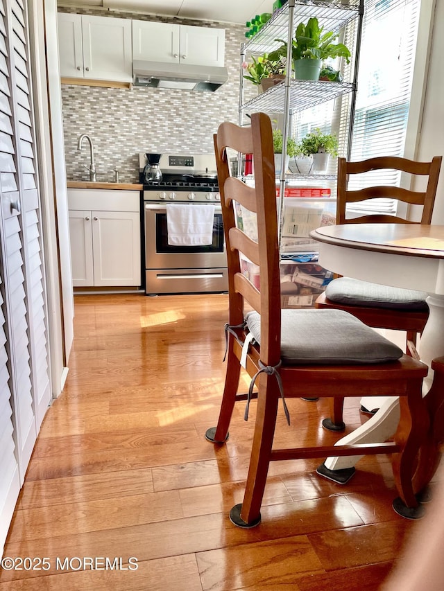kitchen with under cabinet range hood, stainless steel range with gas stovetop, a sink, light wood-style floors, and white cabinetry