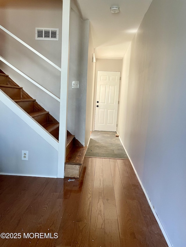 hall with wood-type flooring, baseboards, stairs, and visible vents