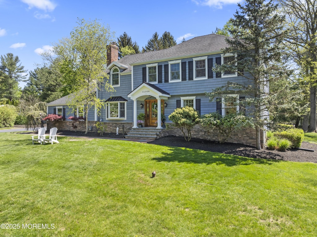 view of front of property featuring a shingled roof, a front lawn, stone siding, and a chimney