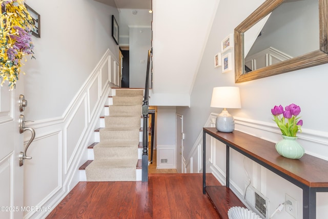 entrance foyer featuring visible vents, wood finished floors, stairway, a wainscoted wall, and a decorative wall