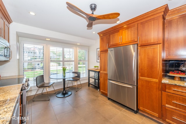 kitchen with brown cabinetry, light stone countertops, ceiling fan, recessed lighting, and stainless steel appliances