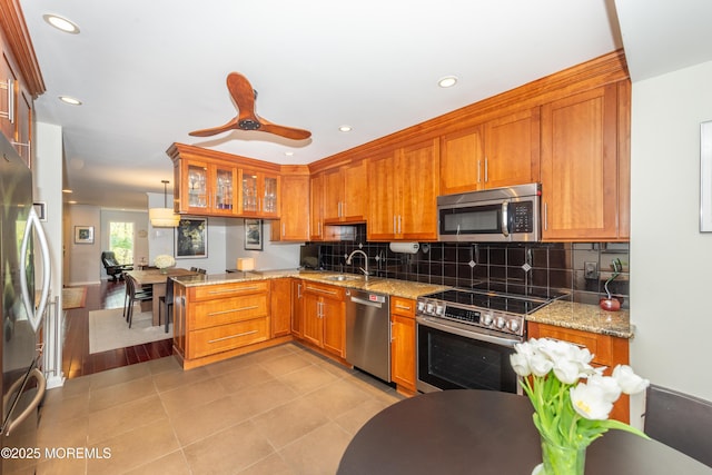 kitchen with a sink, brown cabinetry, stainless steel appliances, recessed lighting, and a peninsula