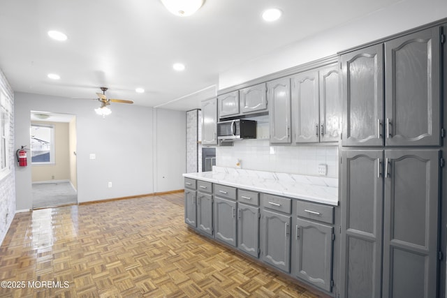 kitchen with light countertops, gray cabinets, baseboards, decorative backsplash, and ceiling fan