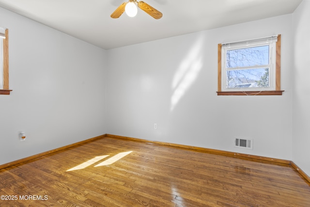 empty room with baseboards, visible vents, hardwood / wood-style flooring, and ceiling fan