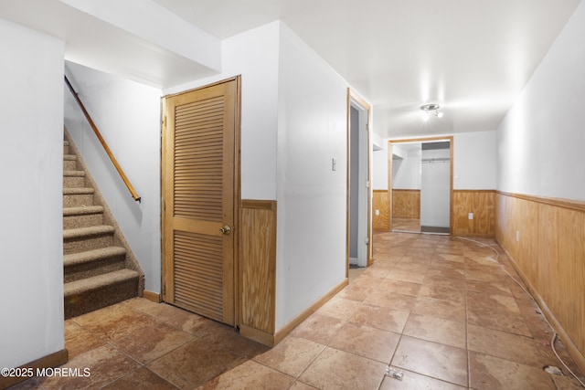 corridor with stone finish flooring, wood walls, stairs, and wainscoting