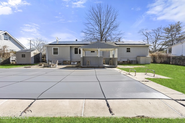 back of property with an outdoor structure, roof mounted solar panels, a yard, and a storage unit