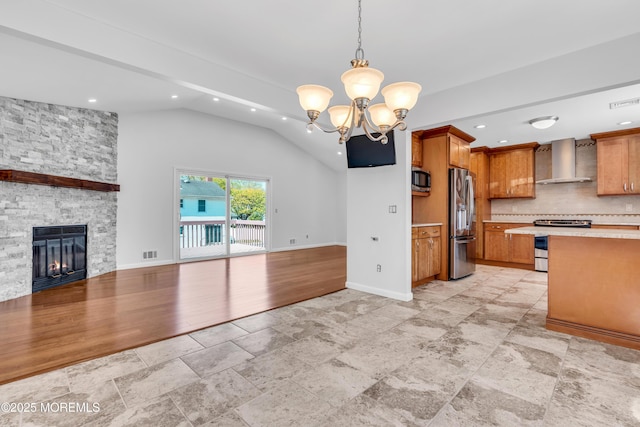 kitchen featuring wall chimney exhaust hood, open floor plan, light countertops, appliances with stainless steel finishes, and lofted ceiling