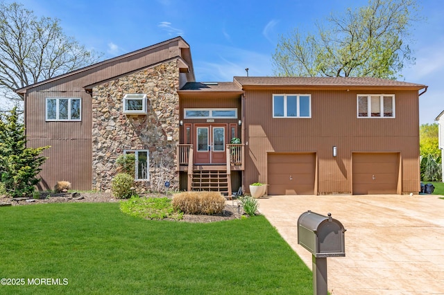 view of front of property featuring driveway, french doors, an attached garage, stone siding, and a front lawn