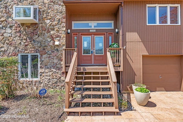 property entrance with a garage, french doors, stone siding, and driveway