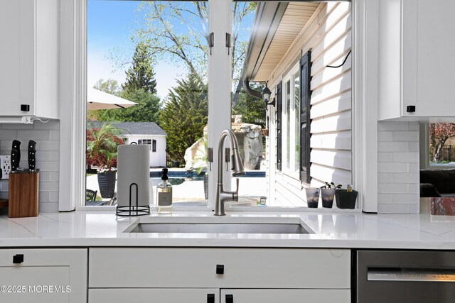 interior space featuring backsplash, dishwasher, white cabinets, and a sink