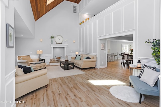 living area with visible vents, wooden ceiling, light wood finished floors, a decorative wall, and high vaulted ceiling
