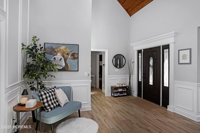 entryway with high vaulted ceiling, wood finished floors, wainscoting, and a decorative wall