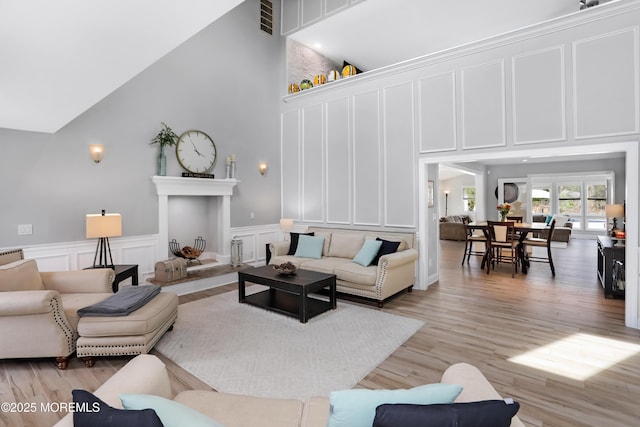living area featuring visible vents, high vaulted ceiling, light wood-type flooring, and a decorative wall