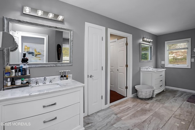 bathroom featuring baseboards, two vanities, marble finish floor, and a sink