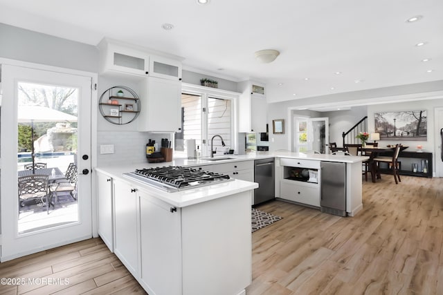 kitchen featuring a sink, stainless steel appliances, glass insert cabinets, a peninsula, and light countertops