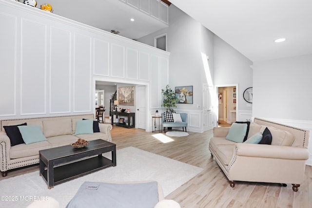 living area featuring recessed lighting, a decorative wall, wainscoting, light wood finished floors, and a towering ceiling
