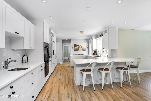 kitchen with recessed lighting, a peninsula, white cabinets, and a sink
