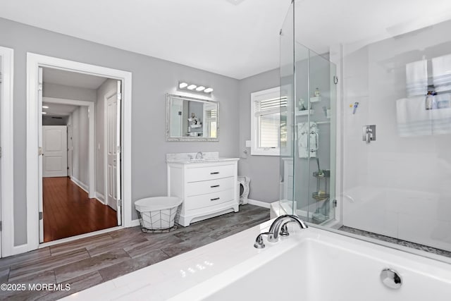 full bath featuring wood finished floors, a shower stall, a tub to relax in, vanity, and baseboards