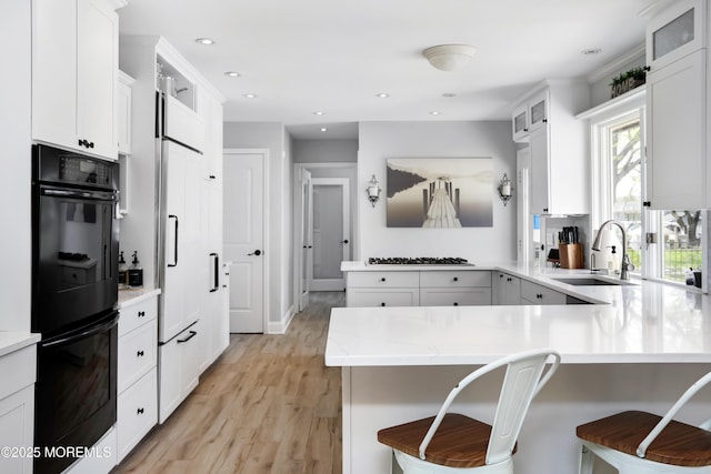 kitchen featuring light wood-style flooring, glass insert cabinets, a sink, gas stovetop, and a peninsula