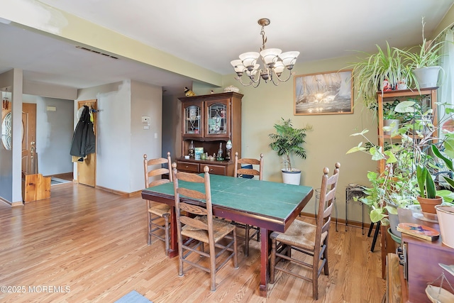 dining area with light wood-type flooring, an inviting chandelier, visible vents, and baseboards