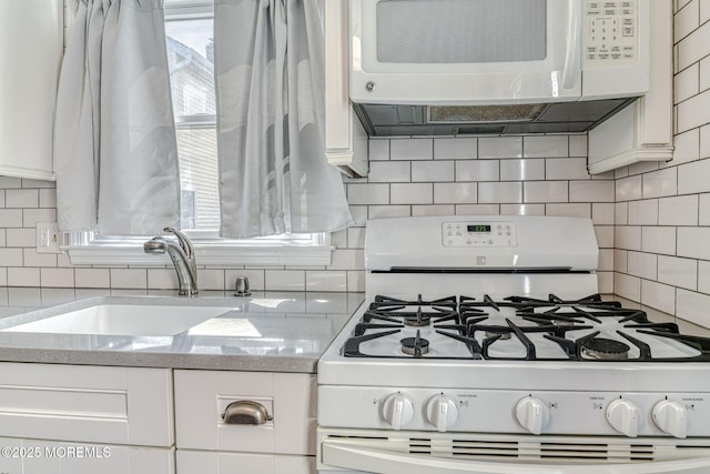 kitchen with white appliances, a sink, backsplash, white cabinets, and light stone counters