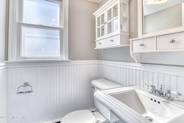 bathroom featuring a sink, toilet, and a wainscoted wall
