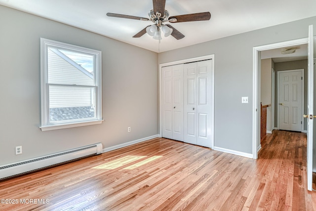 unfurnished bedroom featuring baseboard heating, light wood-style floors, a closet, and baseboards
