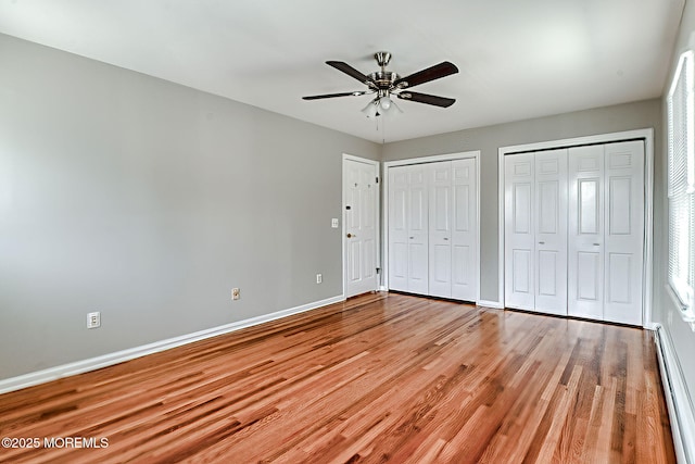 unfurnished bedroom featuring baseboard heating, two closets, baseboards, light wood finished floors, and ceiling fan