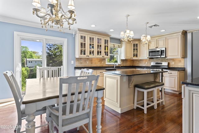 kitchen with cream cabinets, appliances with stainless steel finishes, an inviting chandelier, a center island, and visible vents