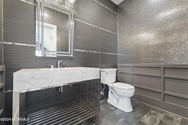 half bathroom featuring vanity, a decorative wall, and toilet