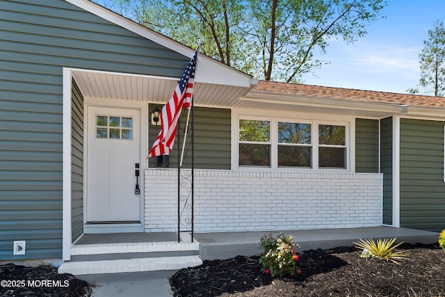 doorway to property featuring brick siding and roof with shingles