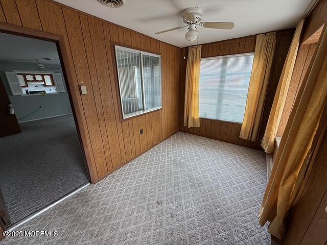 carpeted empty room featuring wood walls and a ceiling fan