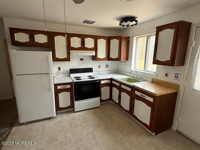 kitchen with freestanding refrigerator, electric range, light countertops, under cabinet range hood, and a sink