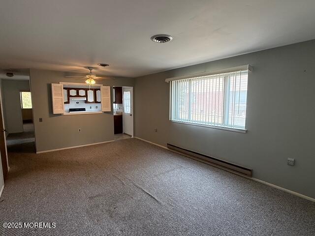 empty room featuring a ceiling fan, a baseboard heating unit, plenty of natural light, and visible vents