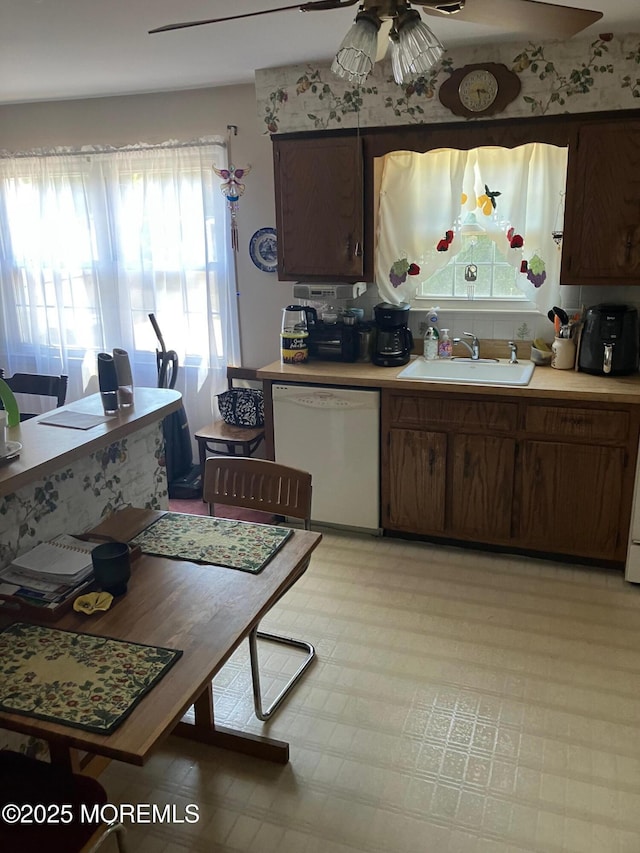 kitchen with white dishwasher, a sink, ceiling fan, light countertops, and backsplash