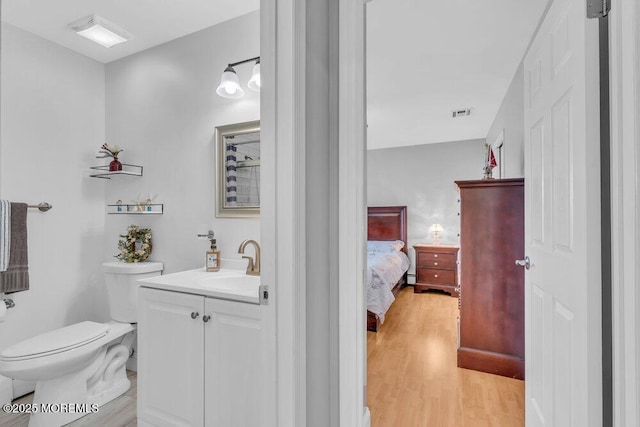 half bathroom with visible vents, wood finished floors, vanity, toilet, and ensuite bathroom