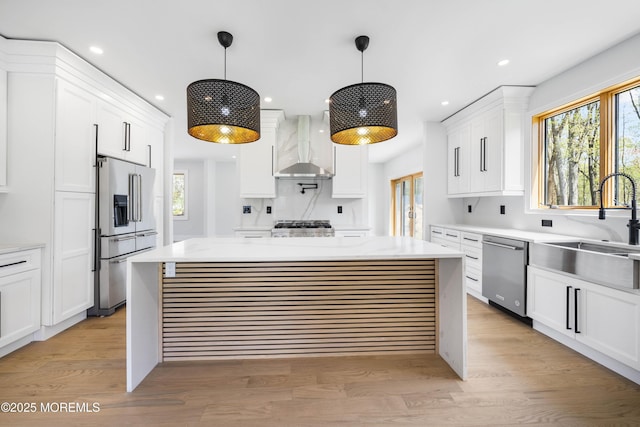 kitchen with a sink, white cabinetry, light countertops, wall chimney exhaust hood, and appliances with stainless steel finishes